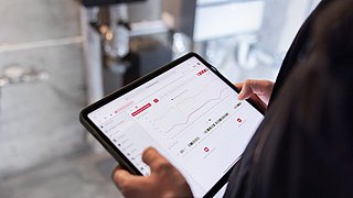 Eine Person hält ein Tablet in der Hand. Auf dem Display sieht man ein Dashboard mit Verbrauchswerten..
